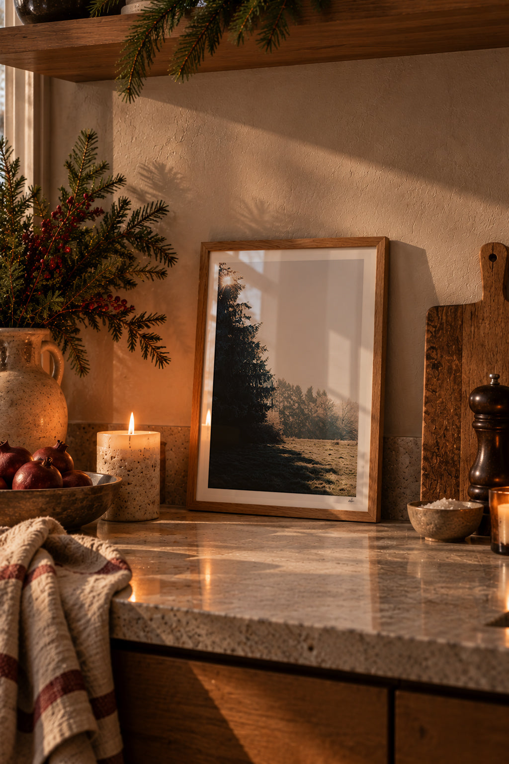 Winter sun through a fir tree over a frosted meadow, Auvergne, France — framed print leaning on a stone kitchen counter beside a candle