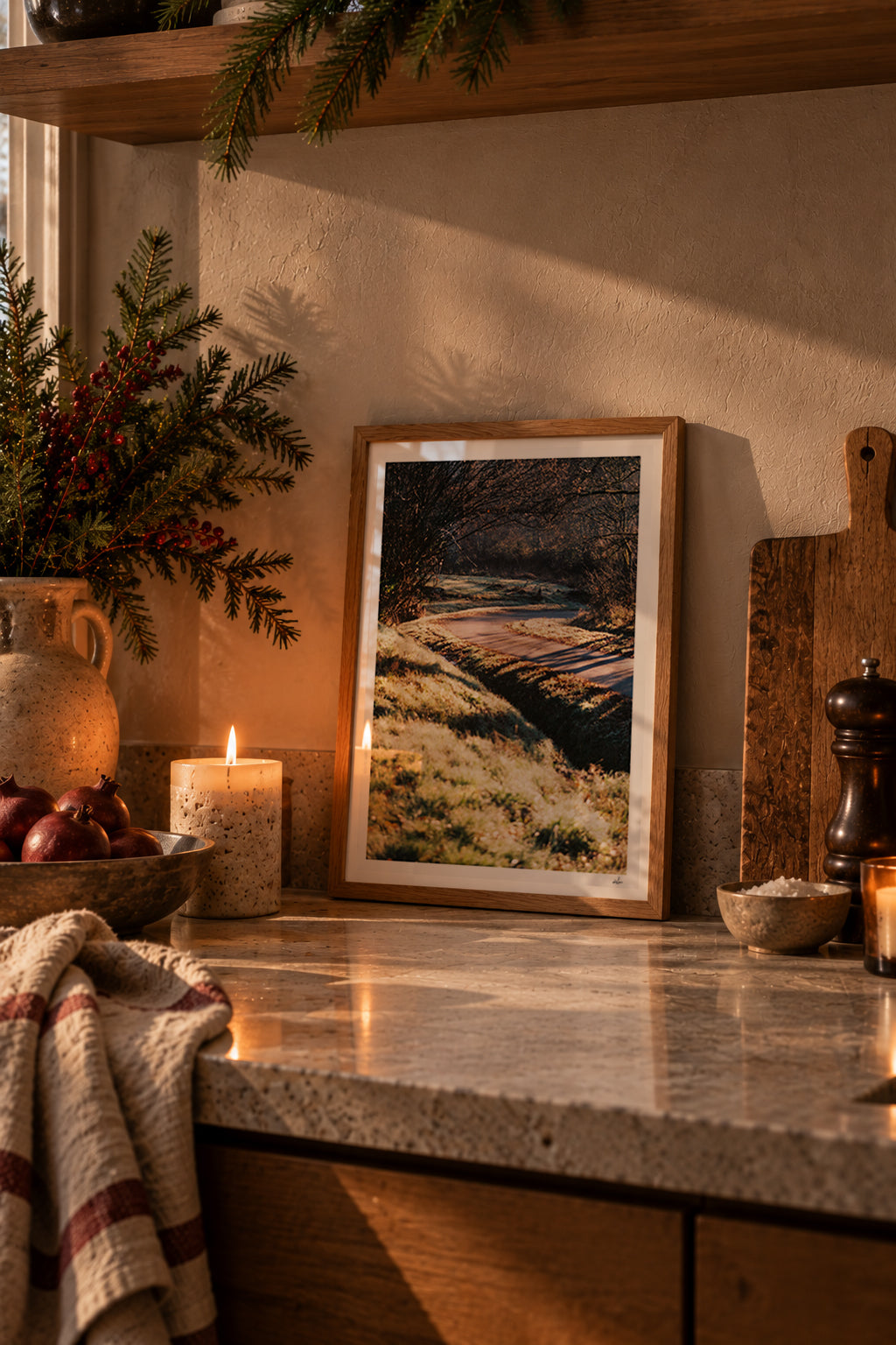 Frosted country lane in low winter sun, Auvergne, France — framed print leaning on a stone kitchen counter beside a candle