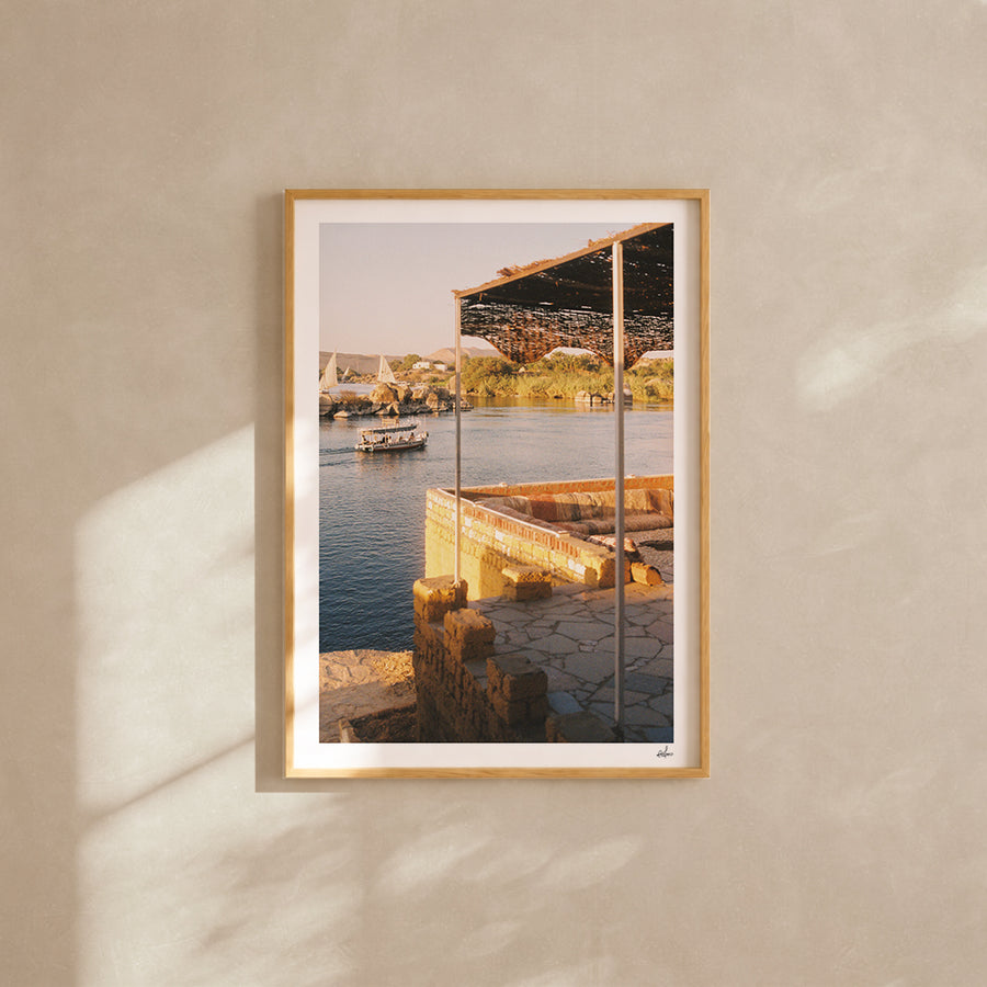 Feluccas on the Nile seen from a shaded riverside terrace, Aswan, Egypt — analog film photography print framed in natural oak